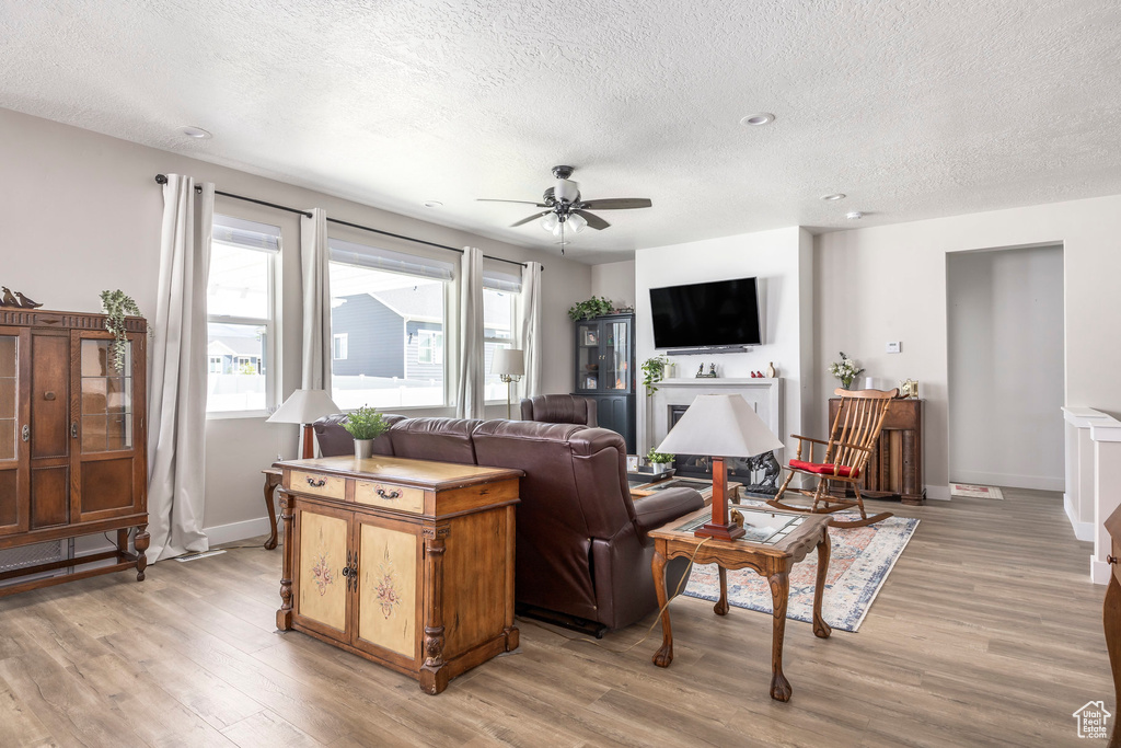 Living room featuring a textured ceiling, light wood-style floors, ceiling fan, and plenty of natural light