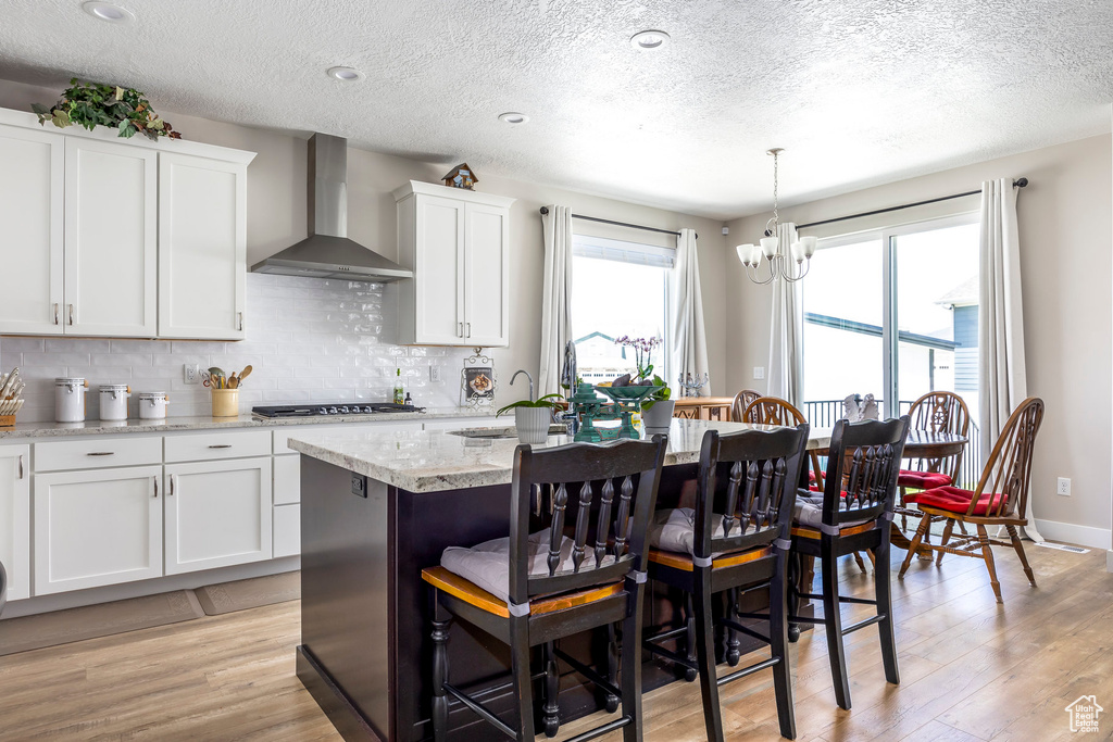 Kitchen with wall chimney range hood, a kitchen bar, light wood-type flooring, gas cooktop, and a chandelier