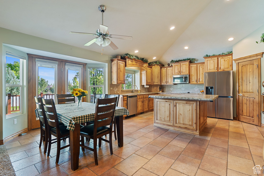 Kitchen featuring appliances with stainless steel finishes, decorative backsplash, a ceiling fan, a center island, and vaulted ceiling