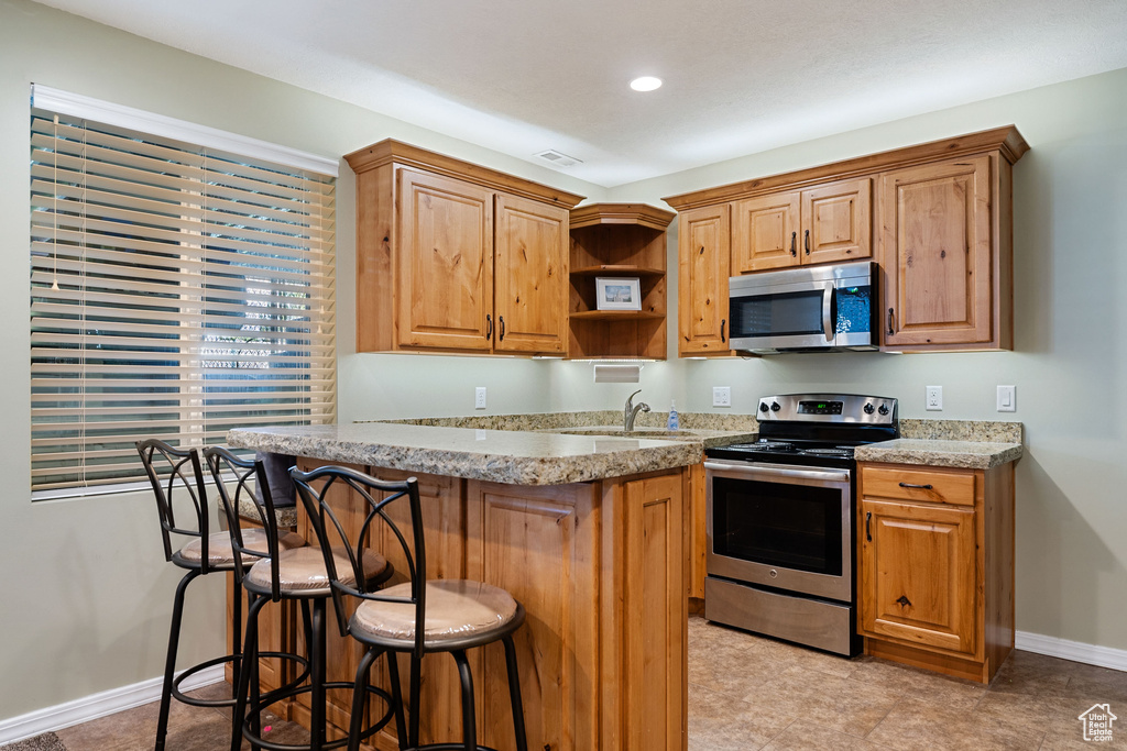 Kitchen featuring stainless steel appliances, a kitchen breakfast bar, open shelves, light stone counters, and recessed lighting
