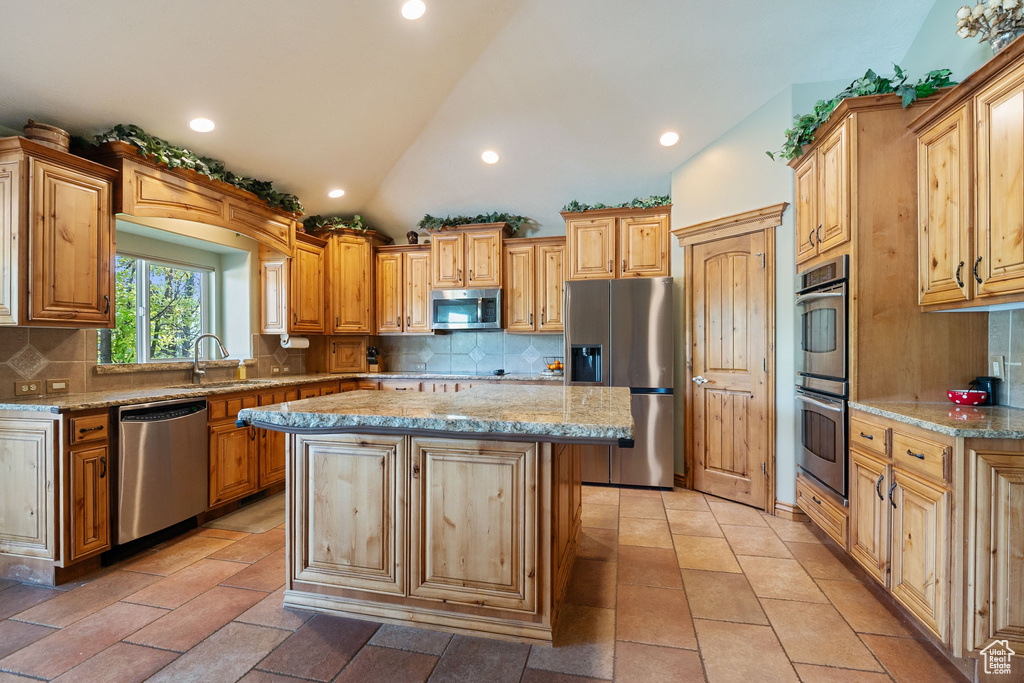 Kitchen with stainless steel appliances, lofted ceiling, light stone counters, tasteful backsplash, and a kitchen island