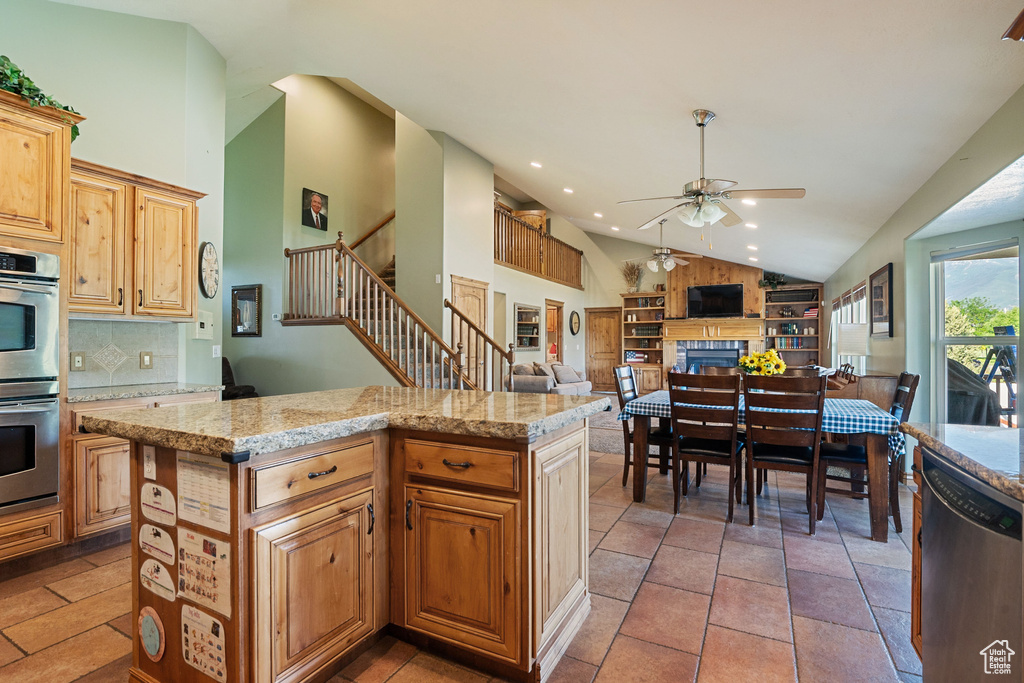 Kitchen featuring stainless steel appliances, a ceiling fan, a fireplace, decorative backsplash, and a kitchen island