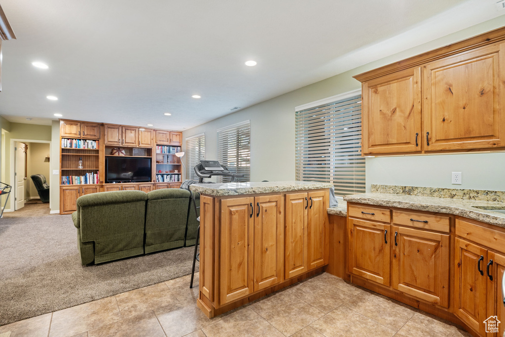 Kitchen featuring recessed lighting, a peninsula, light carpet, light stone counters, and light tile patterned flooring