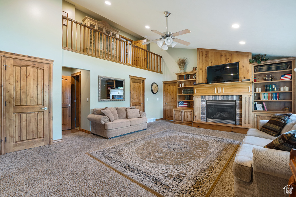 Living area featuring a glass covered fireplace, a ceiling fan, recessed lighting, carpet floors, and a high ceiling