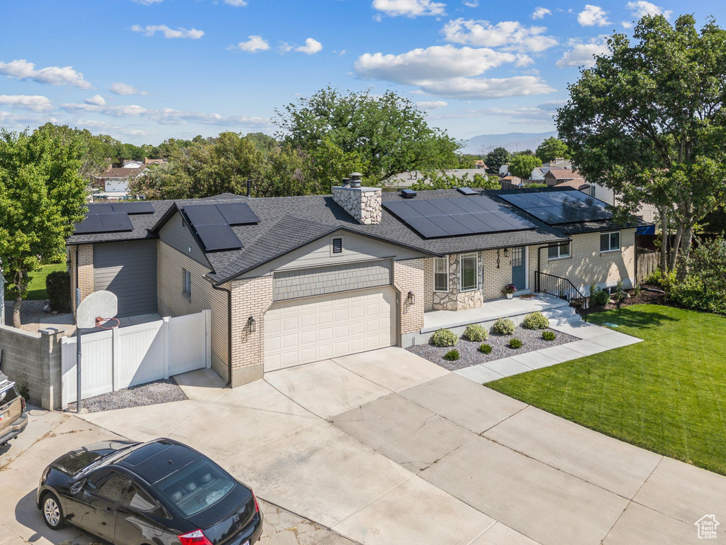 Single story home with an attached garage, solar panels, brick siding, concrete driveway, and roof with shingles