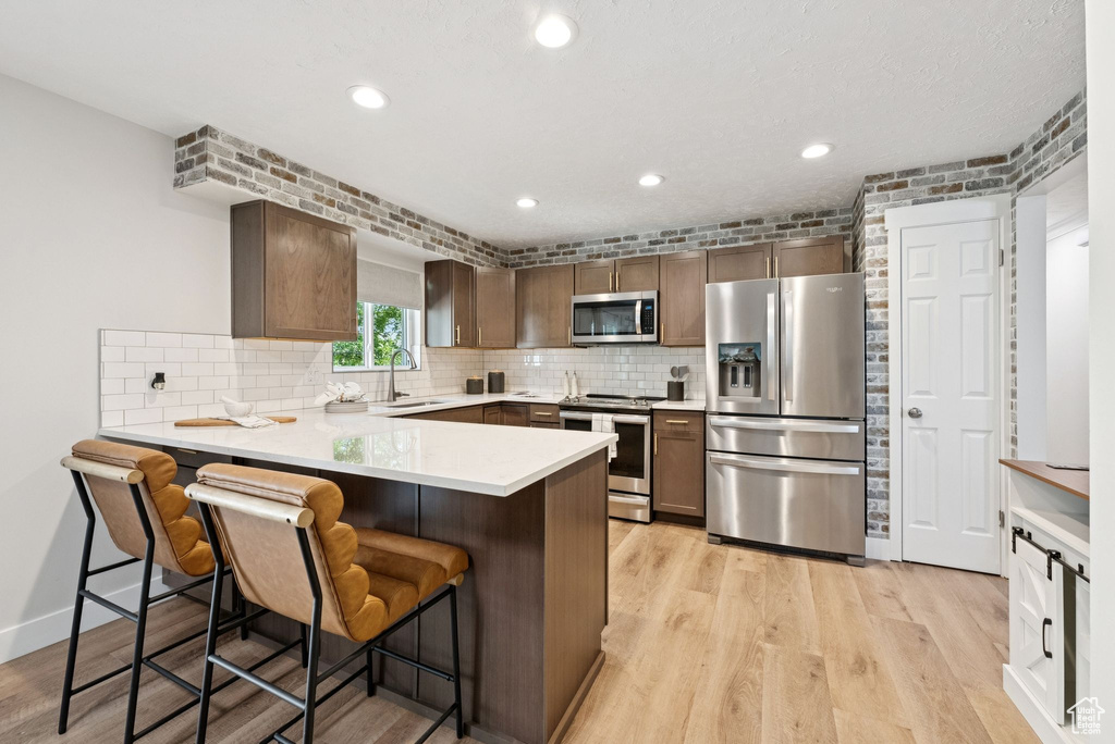 Kitchen featuring stainless steel appliances, a peninsula, light wood-type flooring, decorative backsplash, and recessed lighting