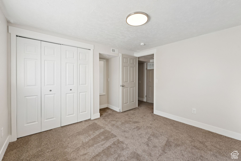 Unfurnished bedroom with carpet floors, a closet, and a textured ceiling