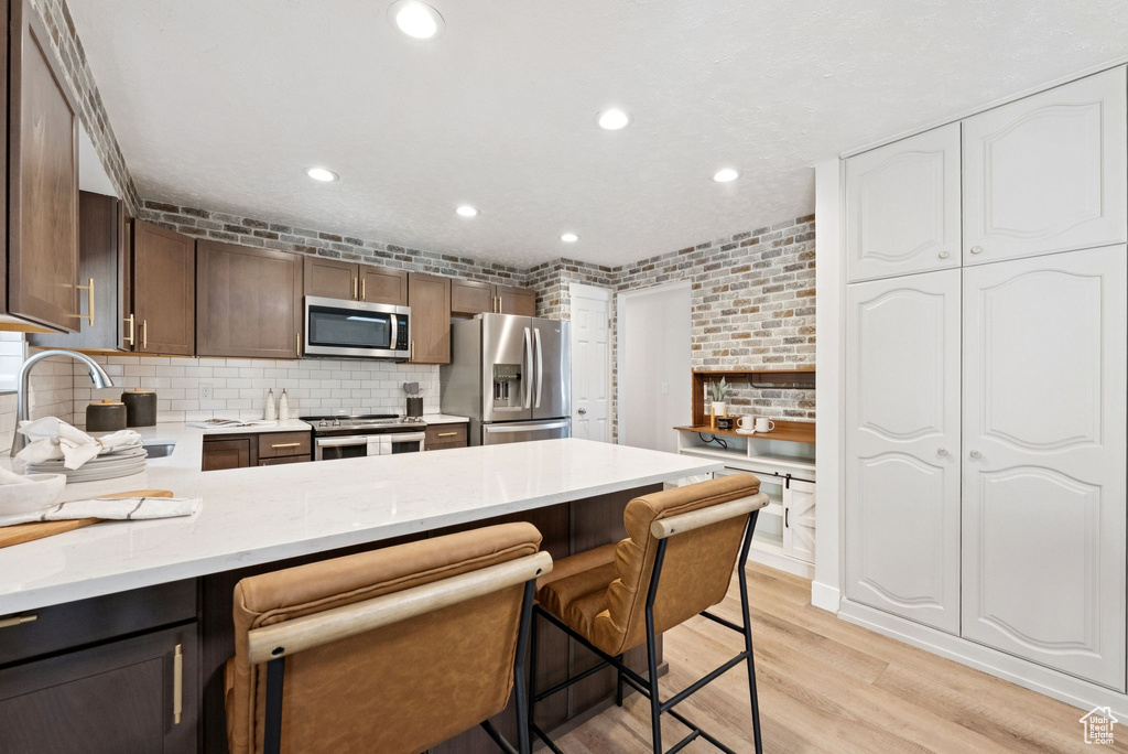 Kitchen featuring stainless steel appliances, light wood-style floors, decorative backsplash, recessed lighting, and a peninsula