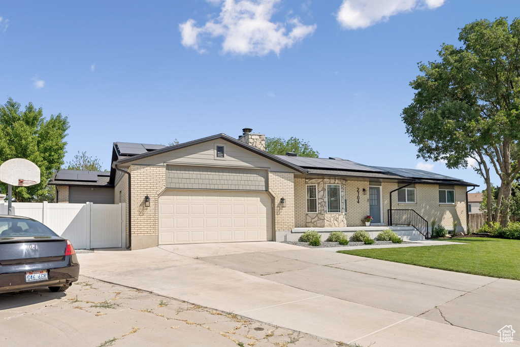 Ranch-style house featuring a garage, driveway, roof mounted solar panels, and brick siding