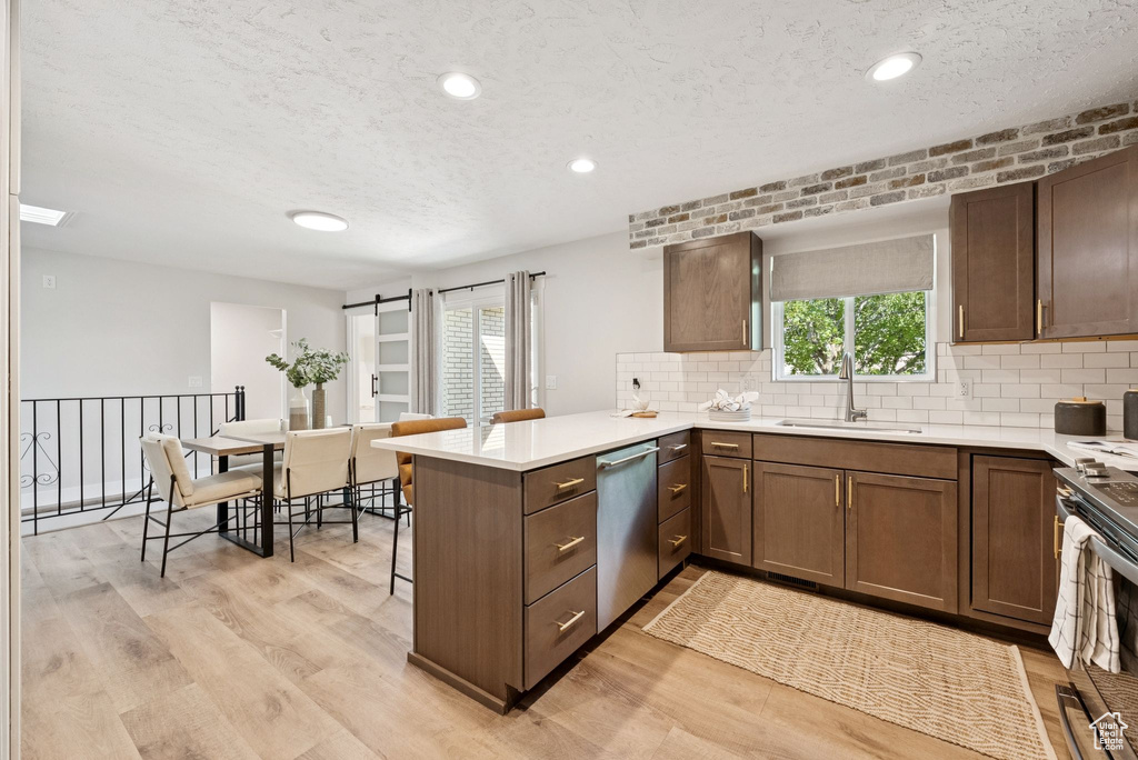 Kitchen with stainless steel appliances, a peninsula, a textured ceiling, light wood finished floors, and decorative backsplash