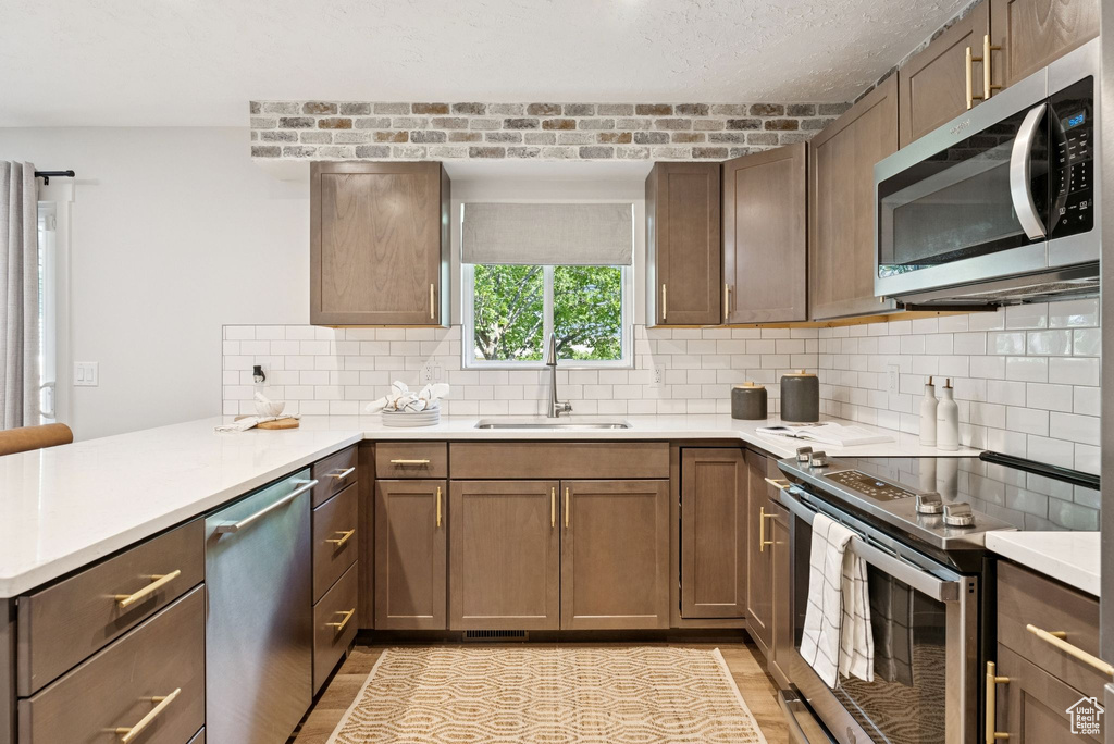 Kitchen featuring stainless steel appliances, a peninsula, light countertops, tasteful backsplash, and light wood-style floors