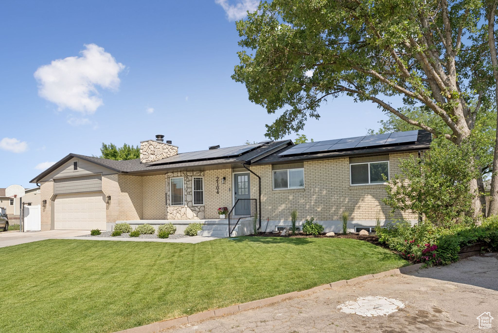 Ranch-style house featuring brick siding, a front yard, driveway, an attached garage, and a chimney