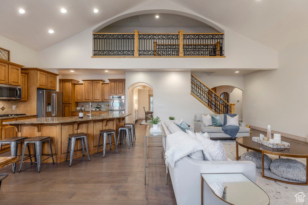 Living room with high vaulted ceiling, arched walkways, wood finished floors, recessed lighting, and stairs
