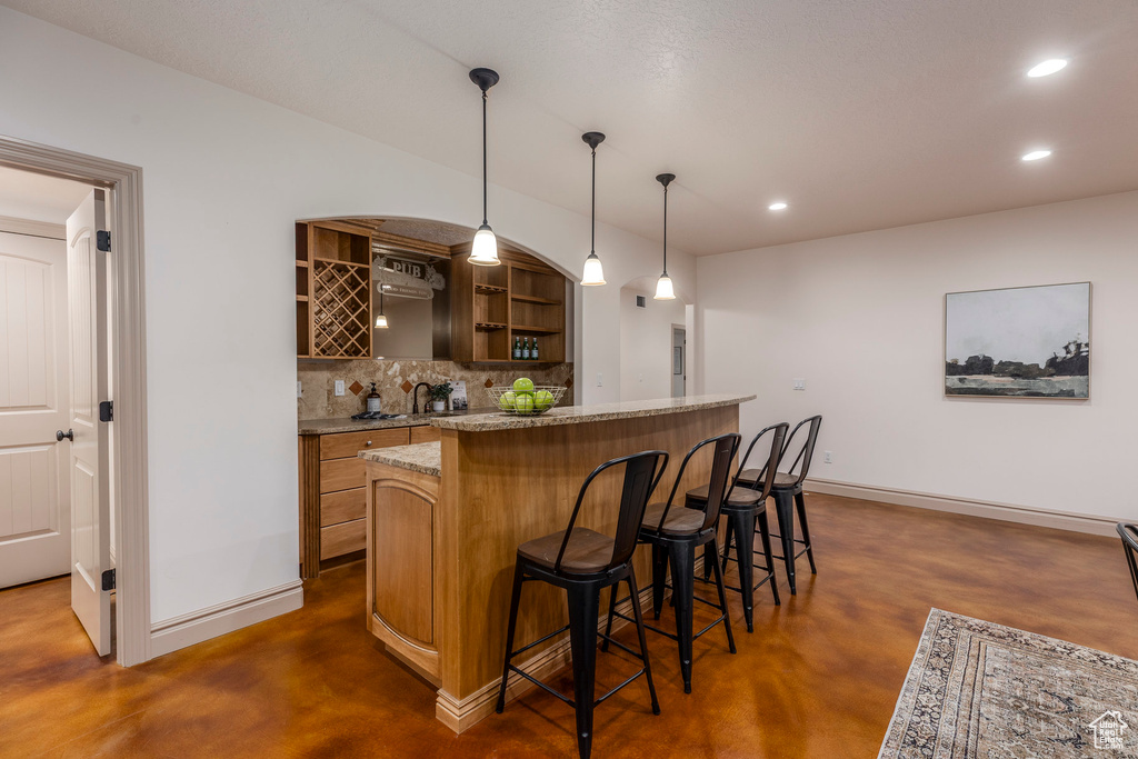 Indoor wet bar with concrete flooring, decorative backsplash, recessed lighting, and decorative light fixtures