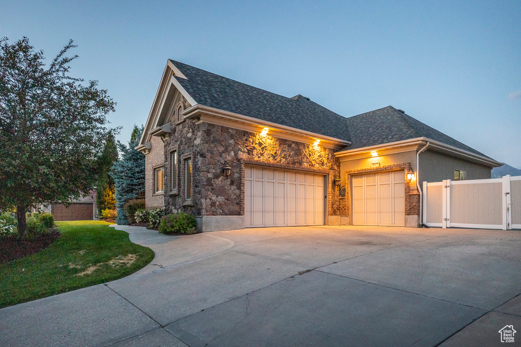 View of side of home featuring stone siding, a garage, concrete driveway, and a shingled roof