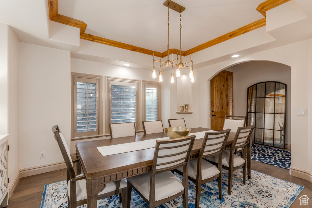 Dining area with wood finished floors, a raised ceiling, arched walkways, and recessed lighting