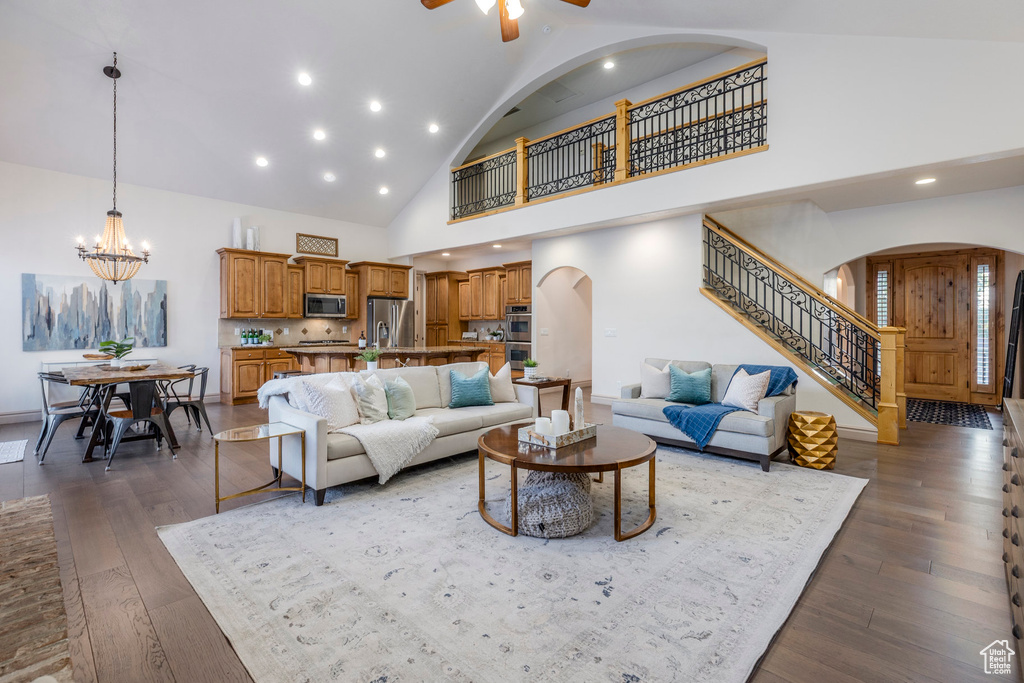 Living area featuring arched walkways, stairway, a chandelier, high vaulted ceiling, and dark wood-type flooring
