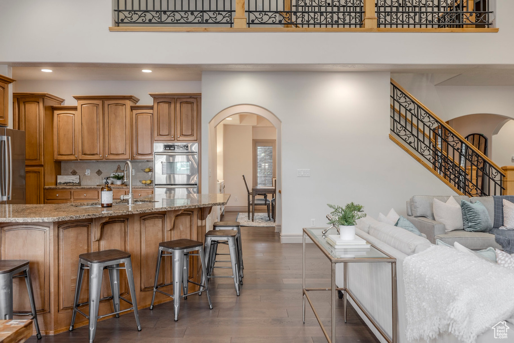 Kitchen featuring arched walkways, a kitchen bar, light stone countertops, wood finished floors, and recessed lighting