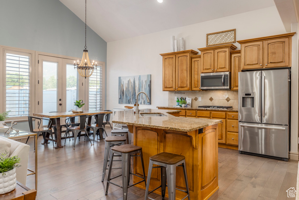 Kitchen with appliances with stainless steel finishes, high vaulted ceiling, light wood-type flooring, light stone counters, and a kitchen bar