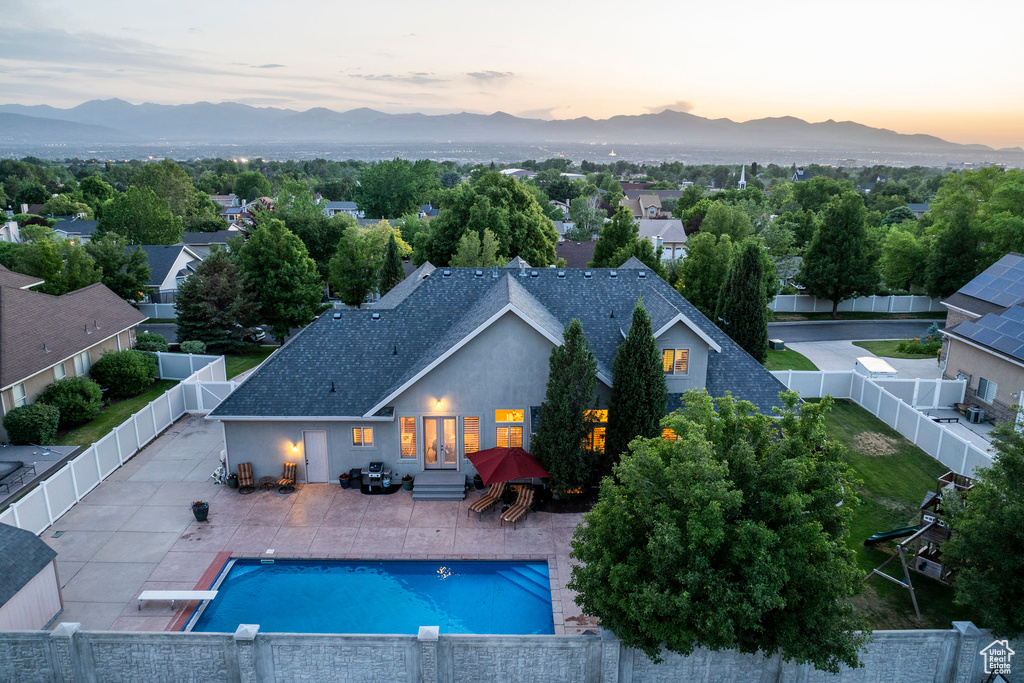 Pool at dusk featuring a mountain view, a fenced backyard, entry steps, a patio area, and french doors