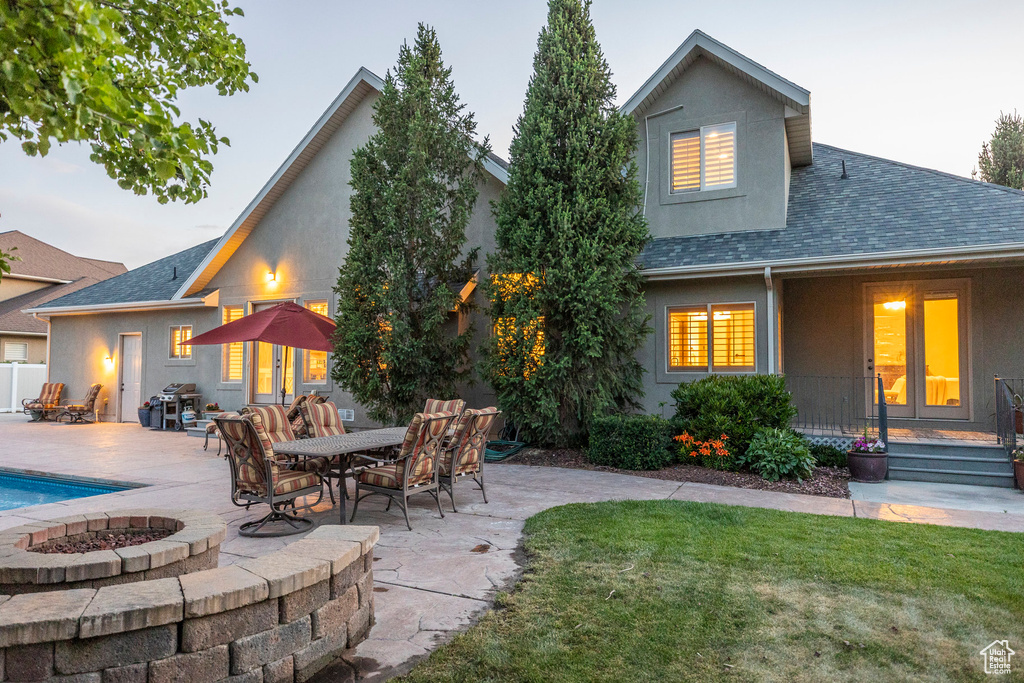 Back of house featuring an outdoor fire pit, roof with shingles, stucco siding, a yard, and a patio area