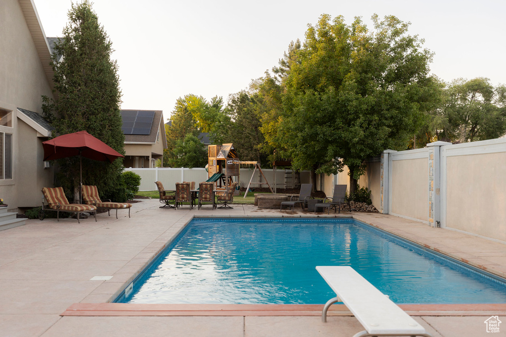 View of swimming pool with a playground, a patio area, a fenced backyard, and a diving board