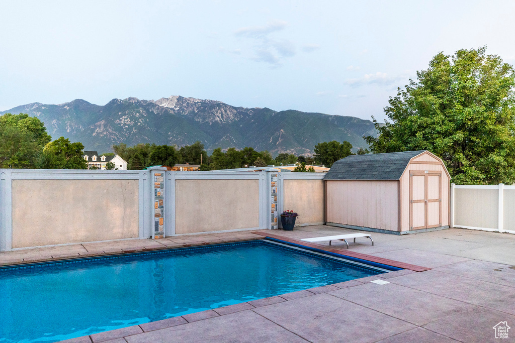 View of pool featuring a storage shed, a patio area, a mountain view, a fenced backyard, and a diving board