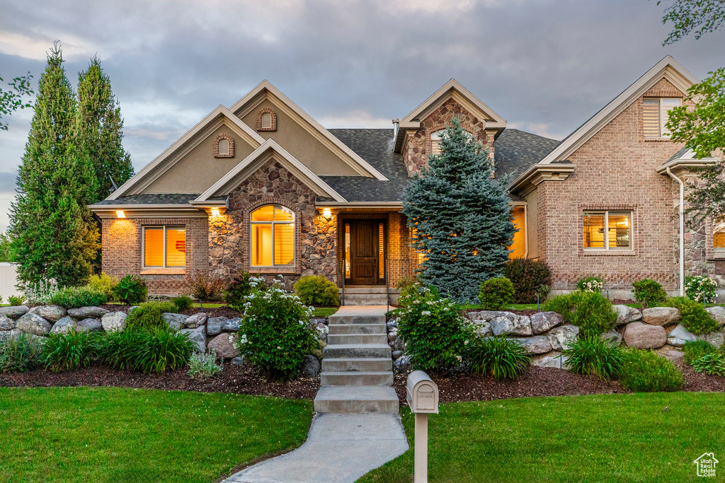 View of front facade with a front lawn, stone siding, stucco siding, brick siding, and roof with shingles