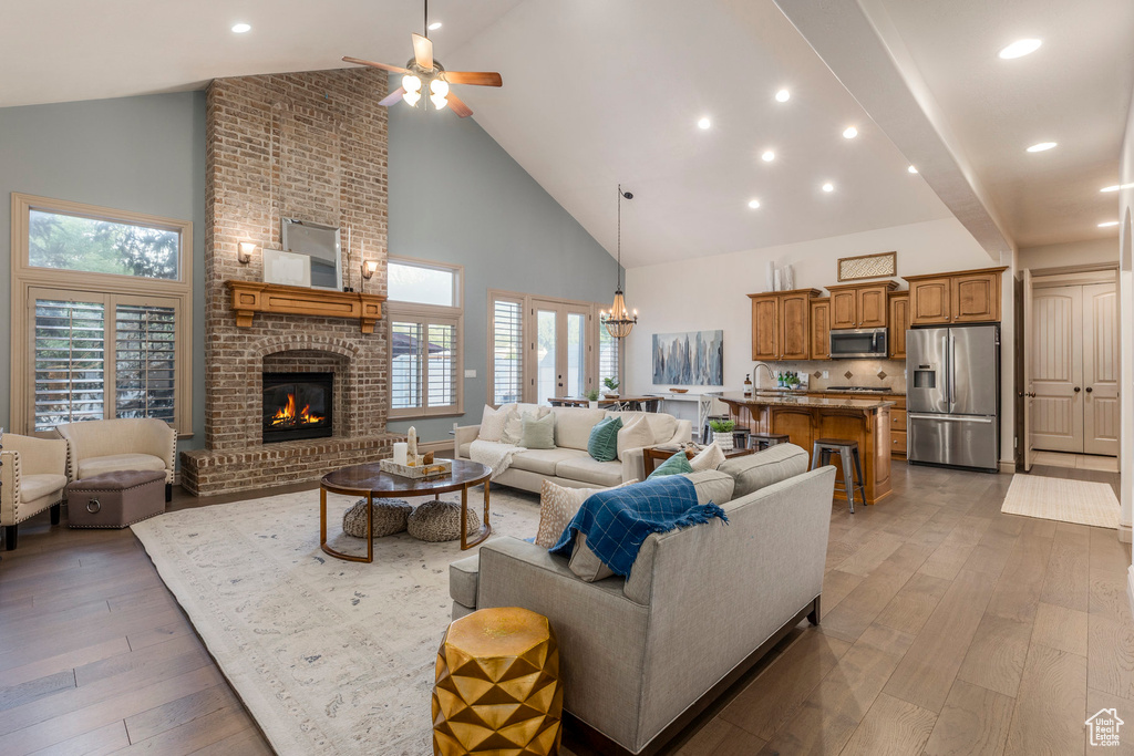 Living room featuring high vaulted ceiling, a ceiling fan, a brick fireplace, light wood-style flooring, and plenty of natural light