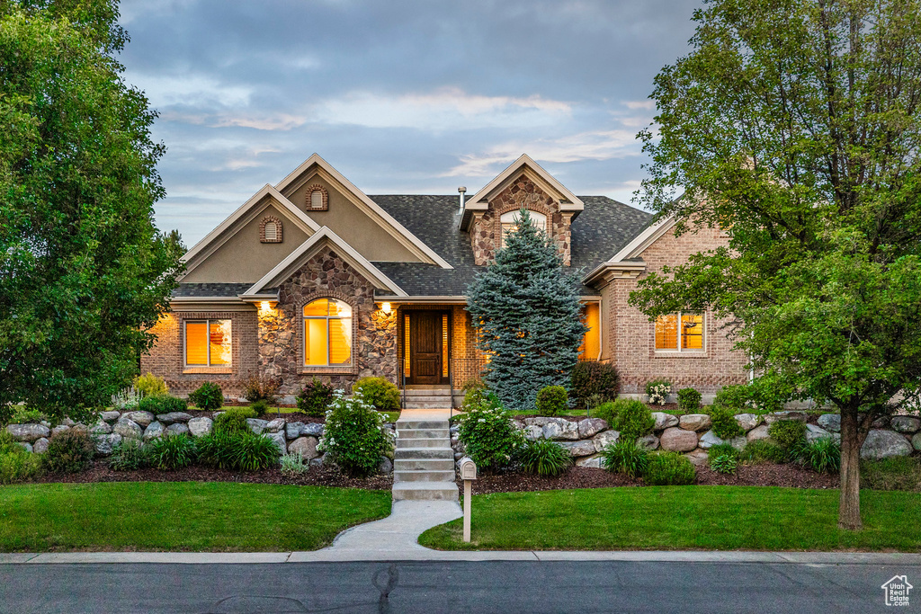 View of front facade with stucco siding, stone siding, a front lawn, and brick siding