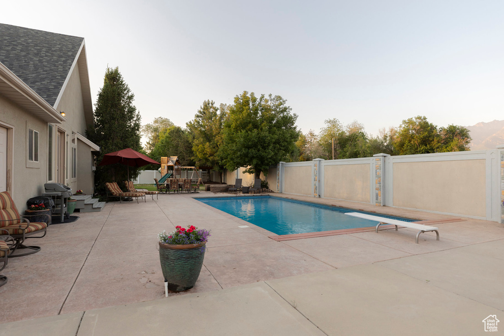 View of pool featuring a playground, a patio, a grill, and a diving board