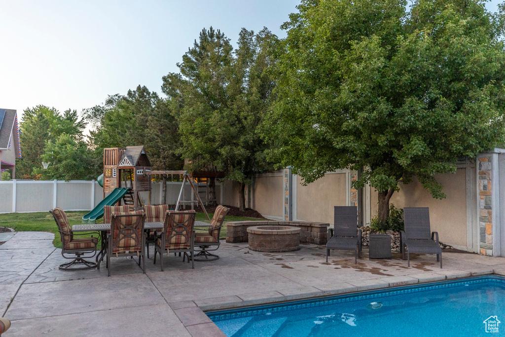 View of pool featuring a playground, a fire pit, a fenced backyard, and a patio area