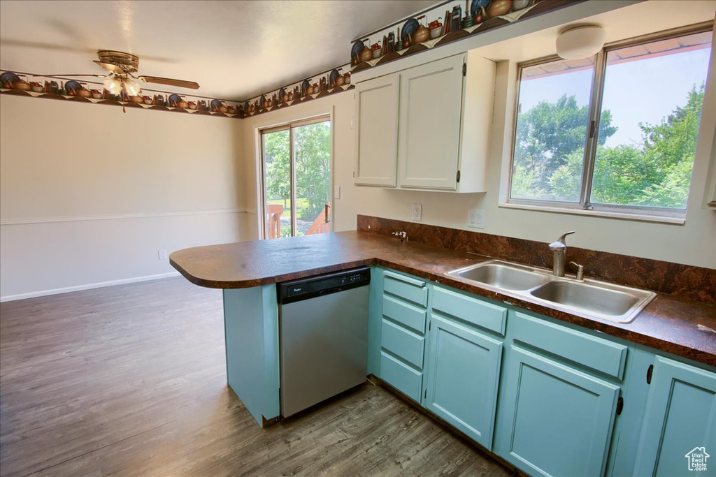 Kitchen with stainless steel dishwasher, dark countertops, a peninsula, blue cabinets, and dark wood-style flooring