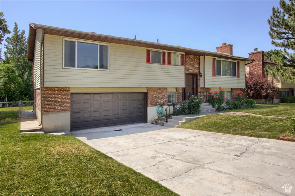 Bi-level home featuring brick siding, a garage, concrete driveway, and a chimney