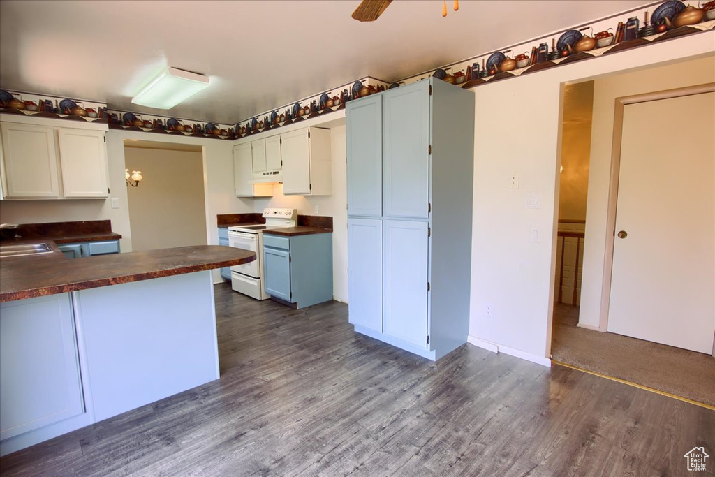 Kitchen featuring white range with electric cooktop, dark countertops, dark wood-style floors, and white cabinetry