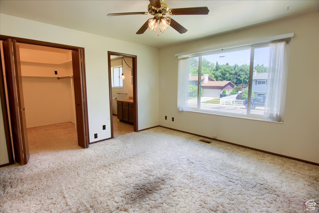 Unfurnished bedroom featuring light carpet, a spacious closet, connected bathroom, a closet, and a ceiling fan