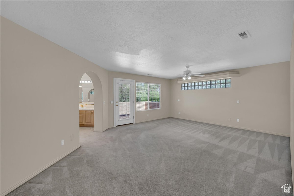 Spare room featuring a ceiling fan, light carpet, plenty of natural light, arched walkways, and a textured ceiling