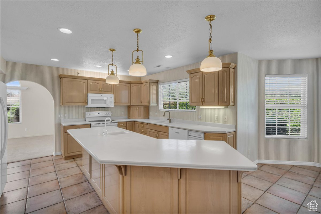 Kitchen featuring white appliances, a kitchen island with sink, light countertops, light brown cabinetry, and a textured ceiling