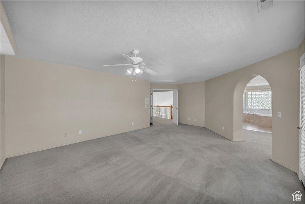 Unfurnished room with arched walkways, ceiling fan, and light carpet