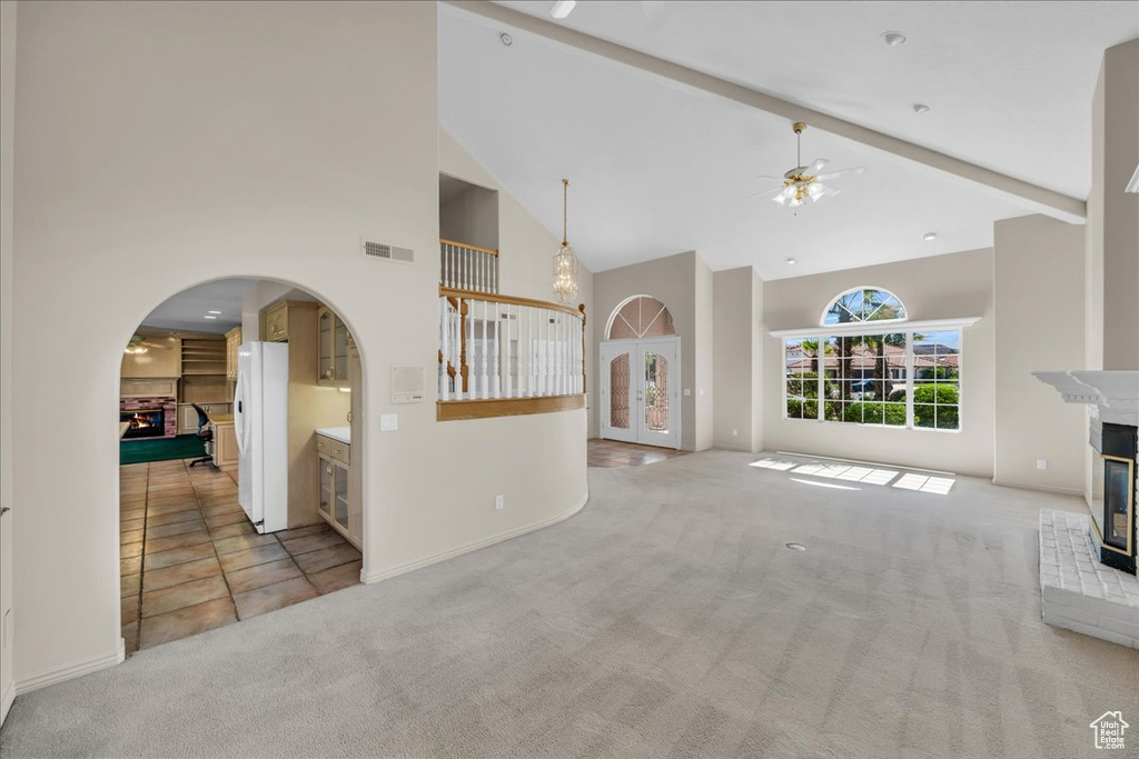 Unfurnished living room featuring a multi sided fireplace, high vaulted ceiling, carpet floors, a ceiling fan, and arched walkways