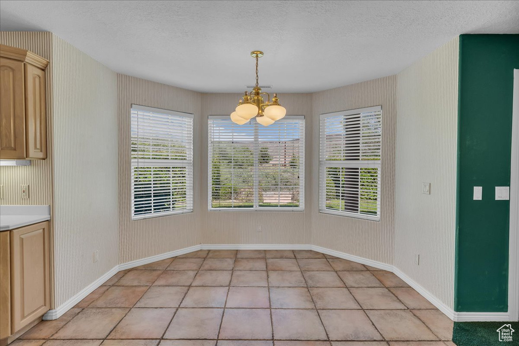 Unfurnished dining area featuring a chandelier, light tile patterned floors, and a textured ceiling