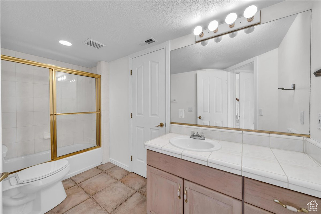 Full bath featuring vanity, a textured ceiling, combined bath / shower with glass door, and tile patterned floors