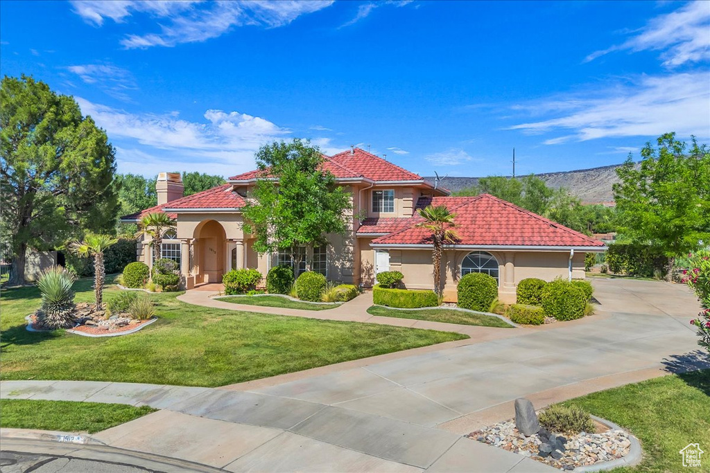 Mediterranean / spanish-style house with stucco siding, a tiled roof, a front lawn, and a chimney