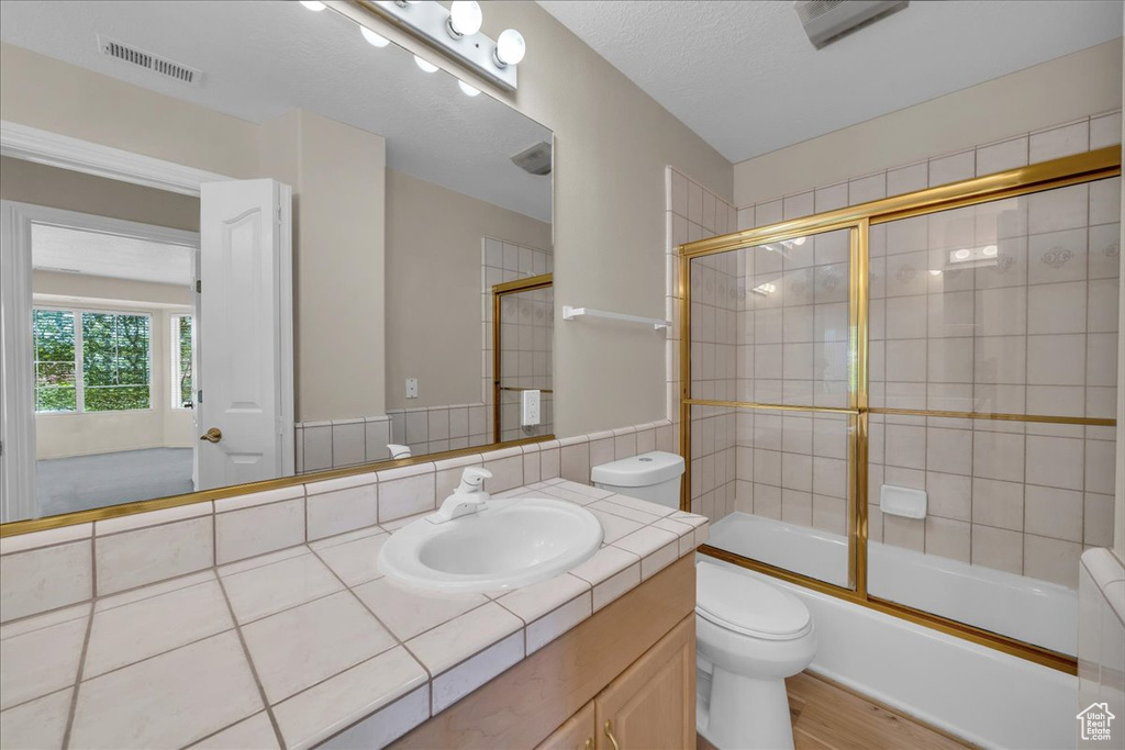 Full bathroom with vanity, wood finished floors, and enclosed tub / shower combo