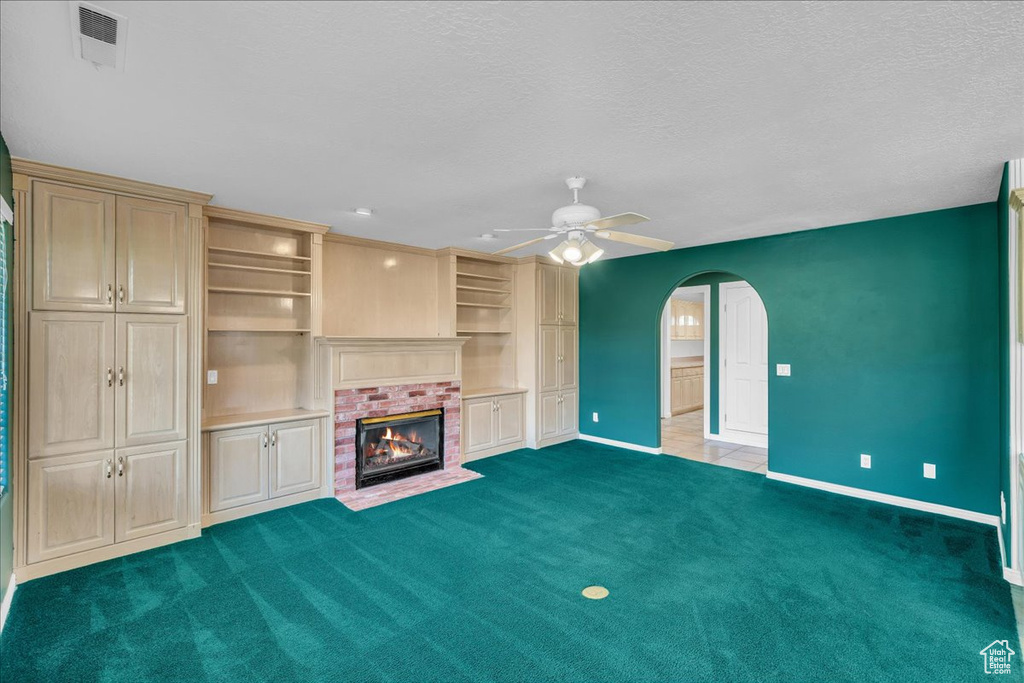 Unfurnished living room featuring arched walkways, ceiling fan, carpet flooring, a fireplace, and a textured ceiling