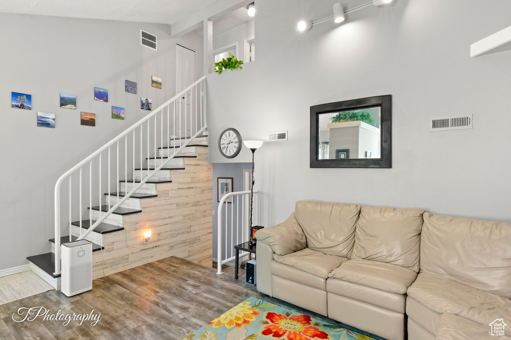Living room with stairs, wood finished floors, high vaulted ceiling, and beamed ceiling