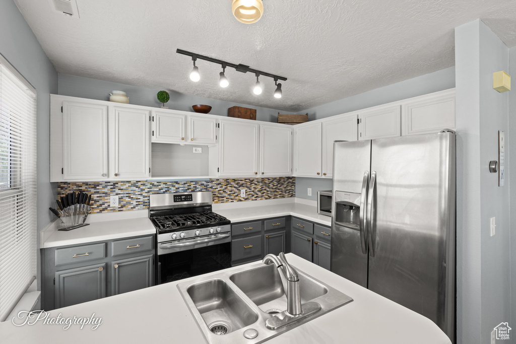 Kitchen with appliances with stainless steel finishes, gray cabinets, white cabinets, light countertops, and decorative backsplash