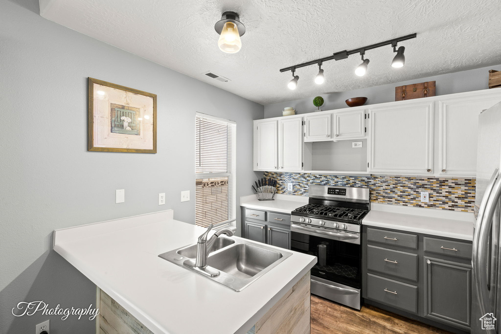 Kitchen featuring stainless steel appliances, wood finished floors, gray cabinets, a peninsula, and a textured ceiling
