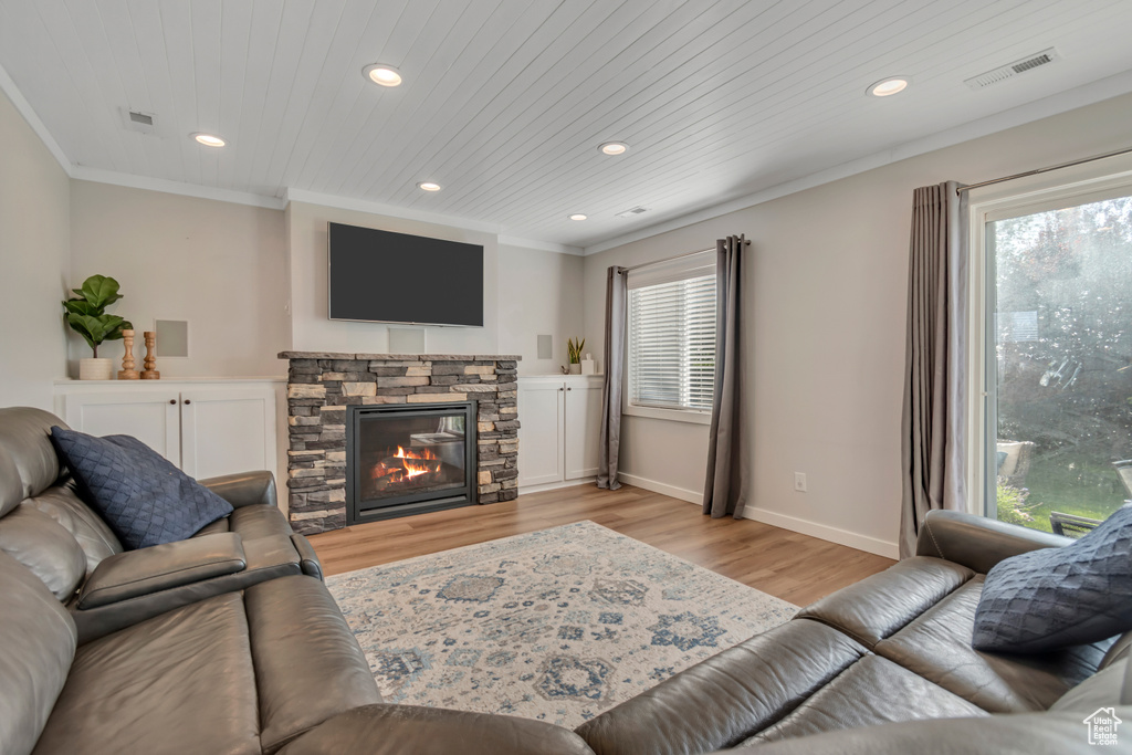 Living area featuring recessed lighting, plenty of natural light, light wood-style flooring, ornamental molding, and a stone fireplace