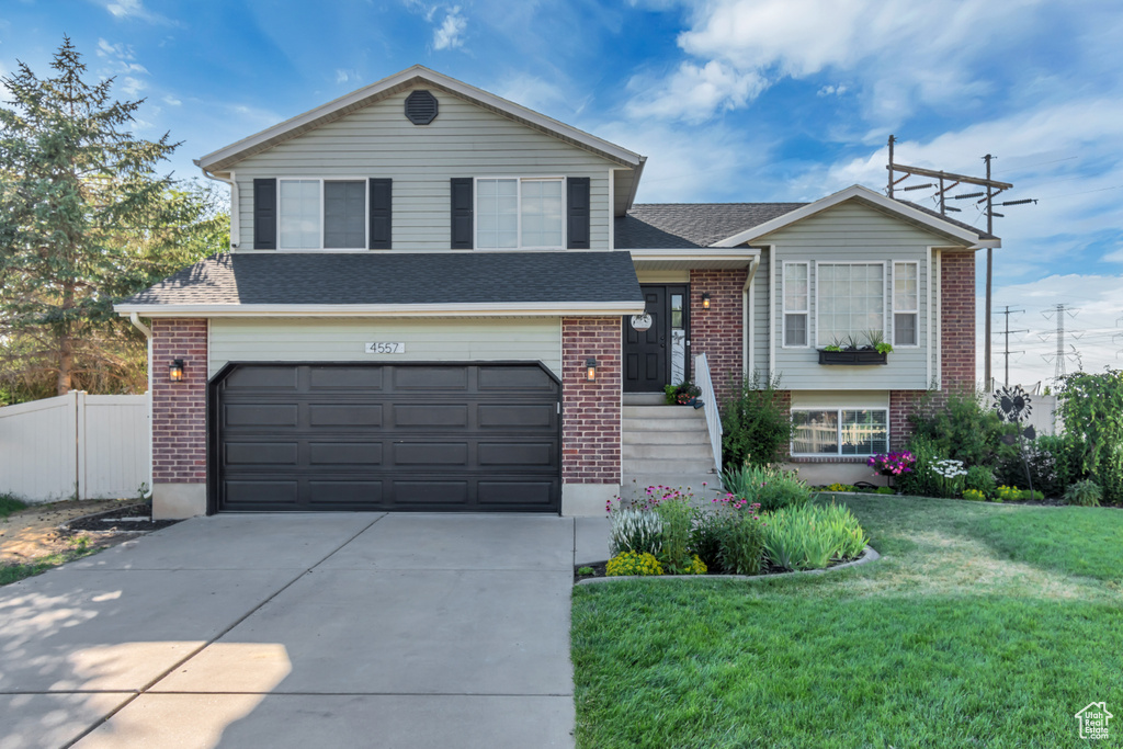 Split level home featuring brick siding, driveway, a garage, and a shingled roof